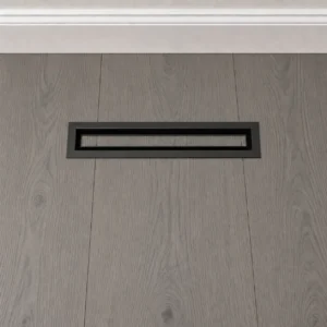 Black narrow floor register installed in gray wood flooring below a baseboard